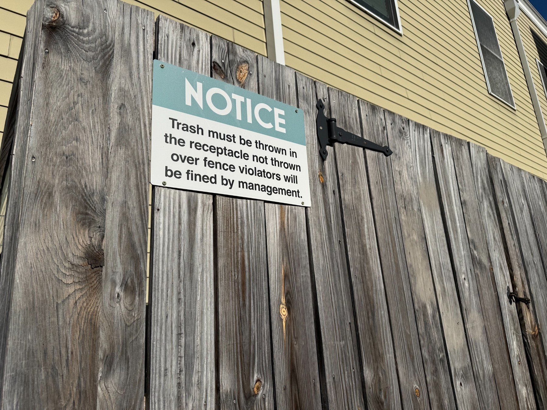 A notice on a wooden fence beside a yellow building
